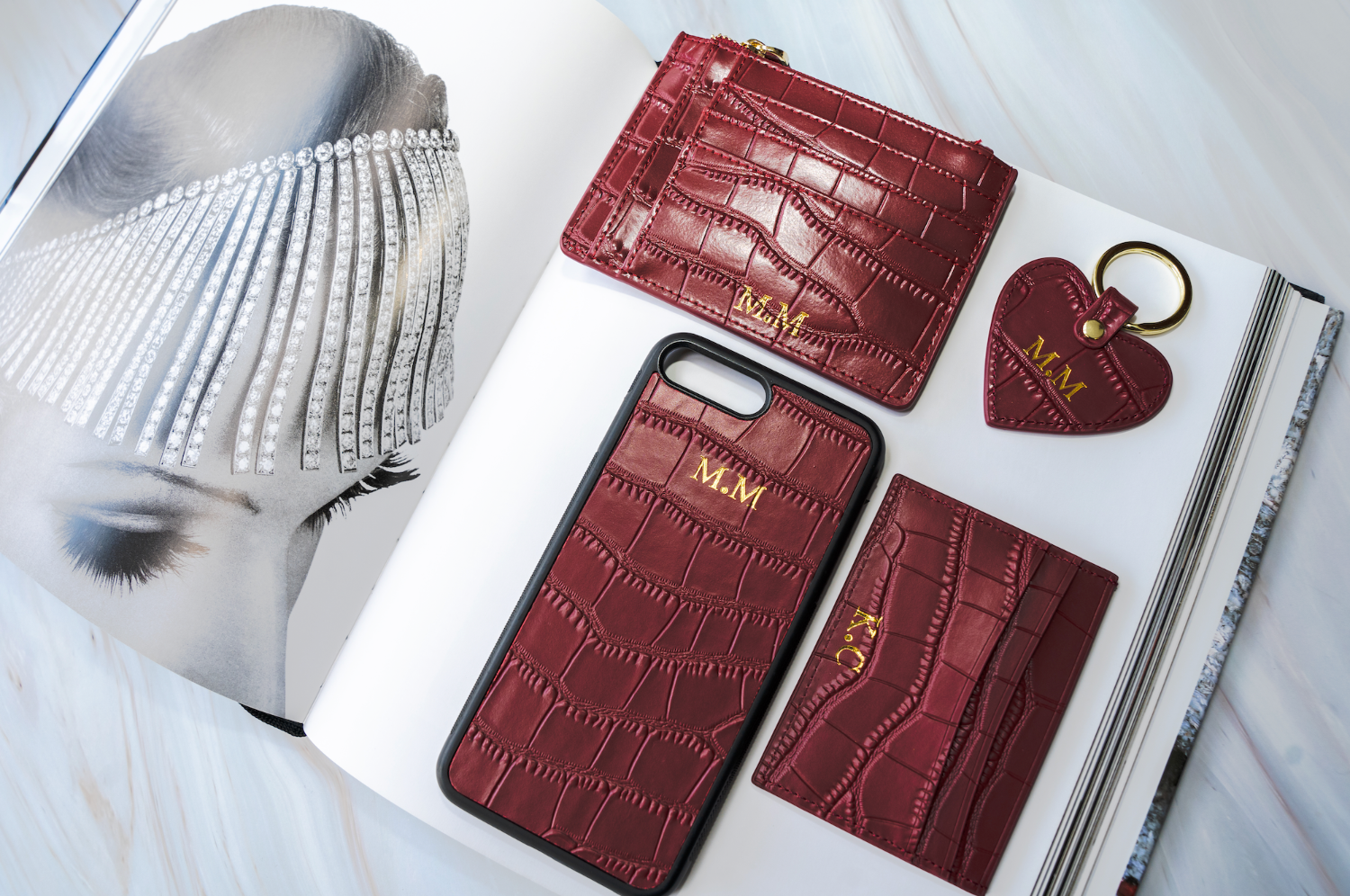 Set of brown leather phone case, cardholder, and keychain on a white surface with a decorative background.